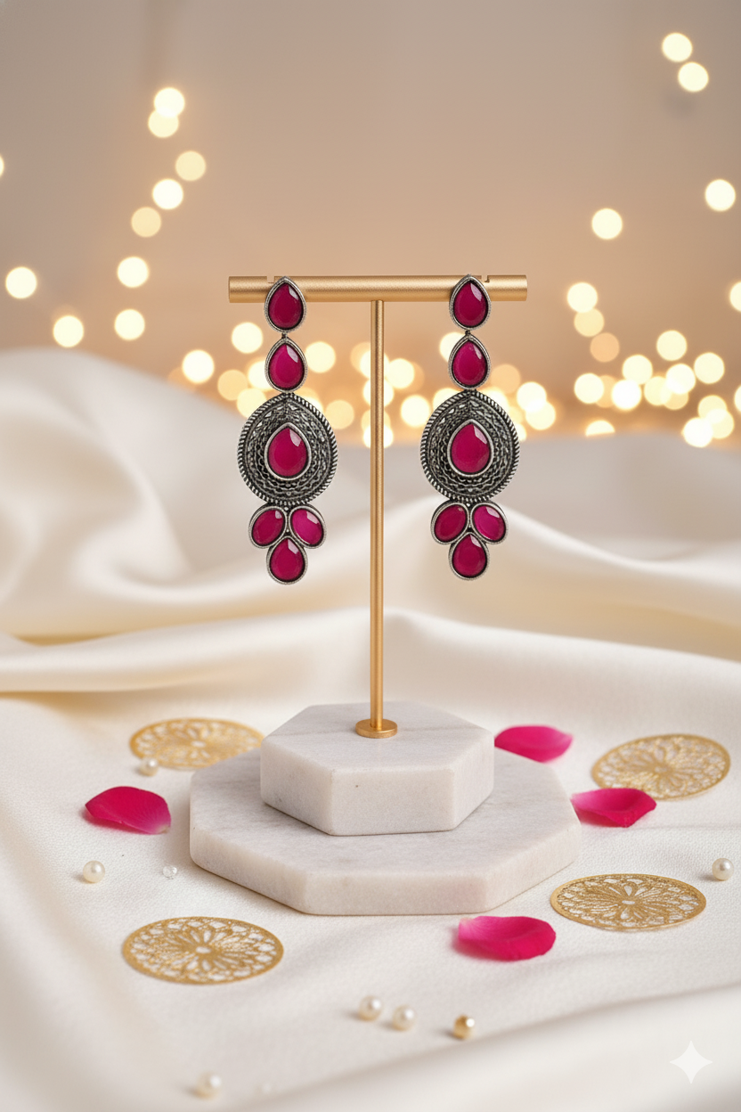 Decorative earrings on a stand with pink gemstones against a soft, blurred light background.