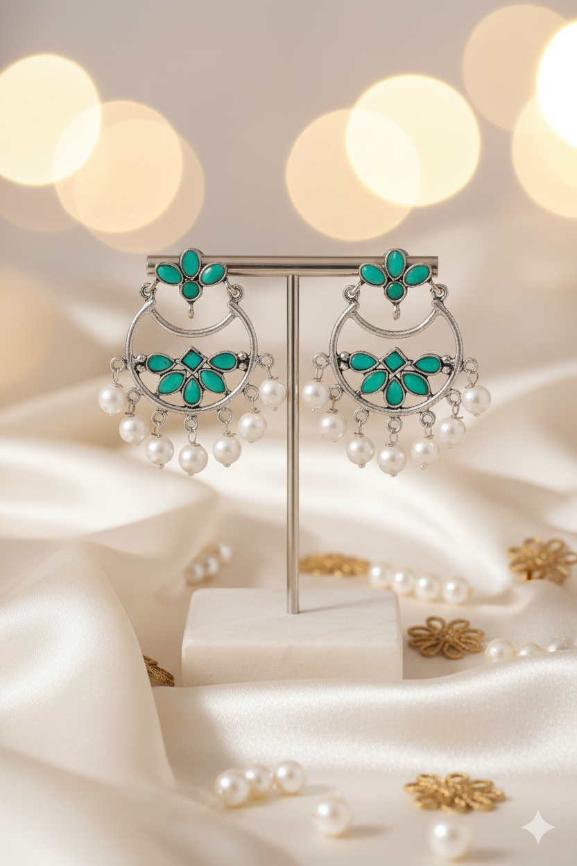 Pair of earrings with turquoise stones and pearl accents on a soft fabric background.